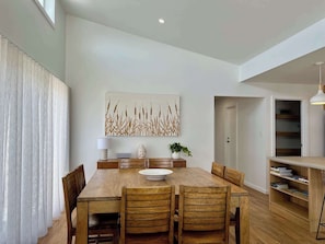 Un comedor con una mesa de madera, sillas, un cuenco blanco, una estatua de Buda, una planta en maceta y una obra de arte colgada en la pared.