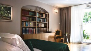A bedroom with a large bookshelf, a bed with a green cover, a chair, and a window with curtains. - Luxury Suite Jasmin-Two Bedroom Suite with Hot Tub (Split)