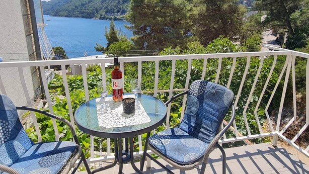 Un balcon avec une table et deux chaises, donnant sur une étendue d’eau et des collines.