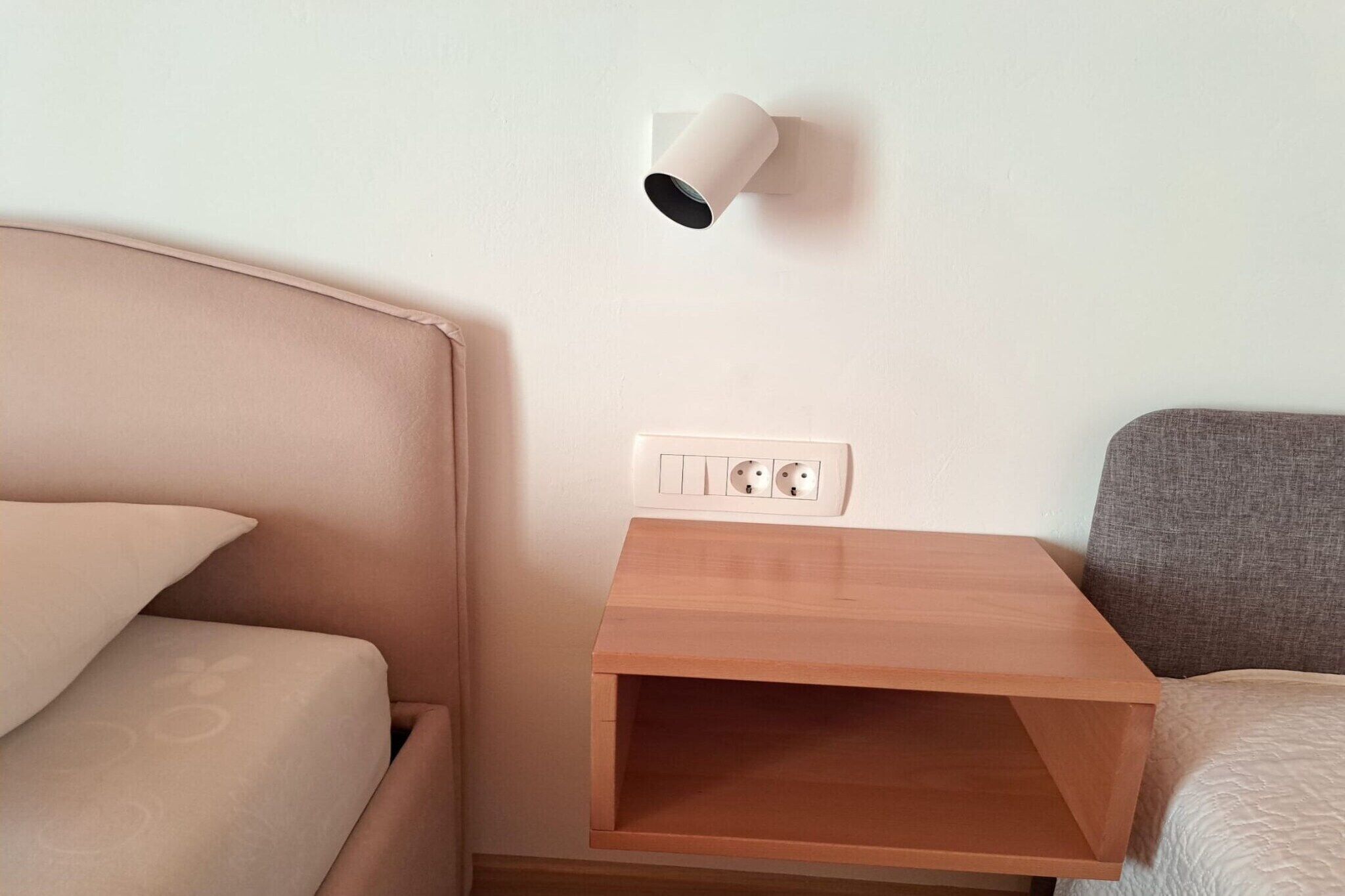 Une chambre à coucher comprenant un lit, une table de chevet, une lampe fixée au mur et une prise de courant.