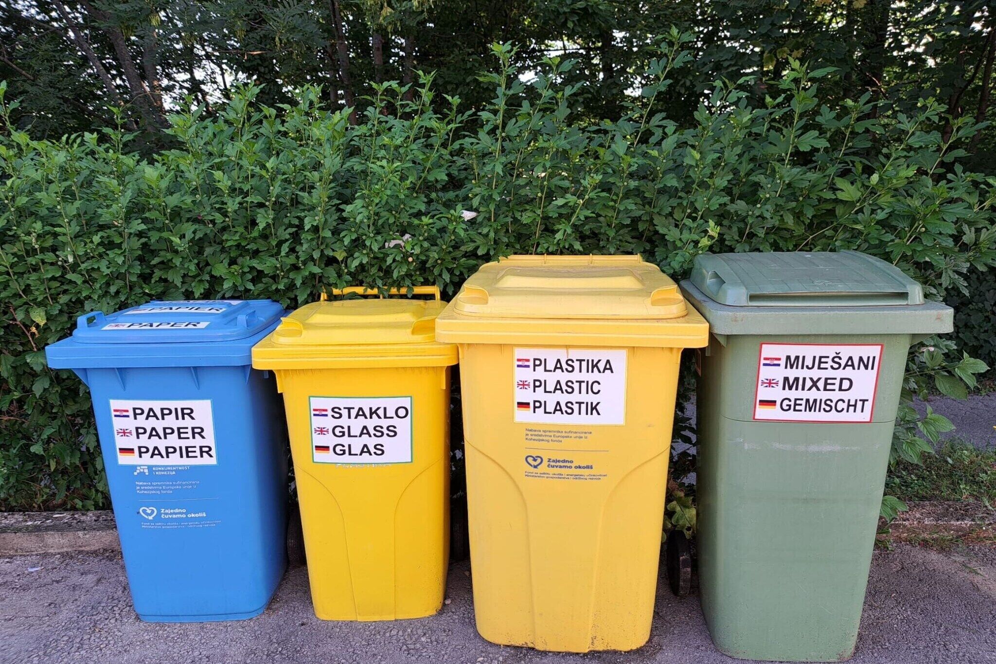 Four waste bins labeled for paper, glass, plastic, and mixed waste.
