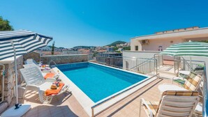 Una piscina sul tetto con acqua cristallina, circondata da poltrone a sdraio e ombrelloni, con vista sulla città.