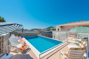 Une piscine sur le toit, avec une eau d’un bleu limpide, entourée de chaises longues et de parasols, offrant une vue panoramique sur la ville.
