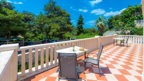 Una terrazza con pavimento a scacchi, arredi esterni e vista su auto parcheggiate e vegetazione.
