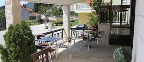 An outdoor patio with tables and chairs, a potted plant, and a view of the surrounding area.