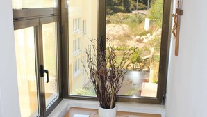 Une pièce d’angle avec un meuble en bois, une plante en pot et une vue sur un bâtiment et la verdure environnante.