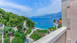 A coastal view with a clear sky, a road leading to the beach, and a building with a balcony overlooking the sea.