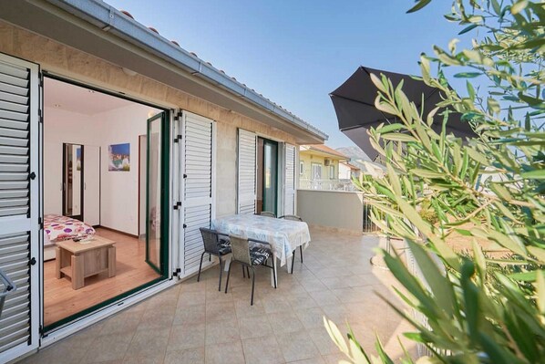 A residential property with a patio area featuring a table and chairs, a small wooden stool, and a bed with a floral bedspread.