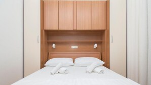 Un lit bien fait, avec du linge de lit blanc, une tête de lit en bois et deux lampes de chevet.