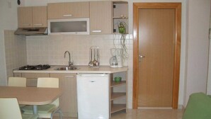 Une cuisine compacte équipée d’un four à micro-ondes, d’une cuisinière, d’un évier et d’un réfrigérateur. On y trouve une table à manger avec des chaises, ainsi qu’un canapé vert dans l’espace salon.