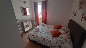 Un dormitorio con cama, mesita de noche, cómoda, espejo y ventana con cortinas.