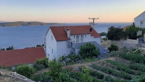 Un edificio costero con techo de tejas rojas, fachada blanca y vista al mar.