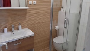 Un baño con tocador de madera, lavamanos, inodoro y cabina de ducha de vidrio.