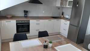 Una cocina moderna con armarios blancos, horno integrado, refrigerador de acero inoxidable y una mesa de comedor con individuales.