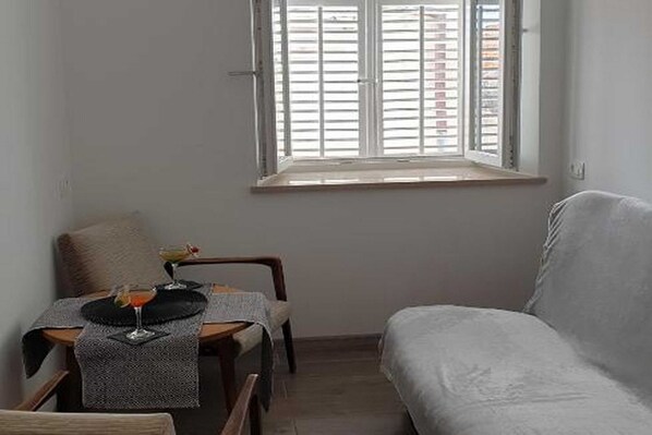 A small, cozy room with a single bed, a table with two glasses, and a window with blinds.