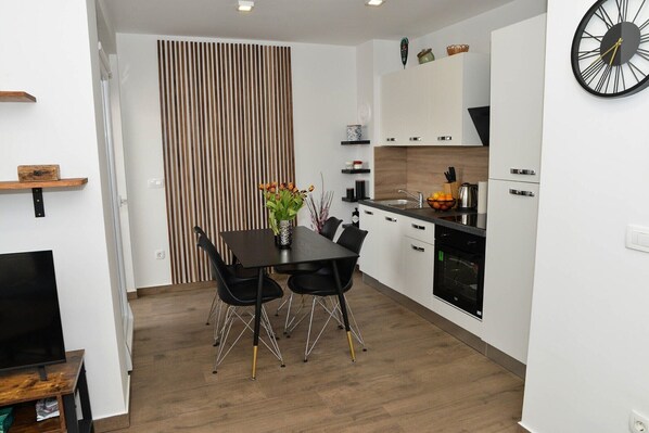 A modern kitchen with white cabinets, a black countertop, and a dining area with a black table and chairs.