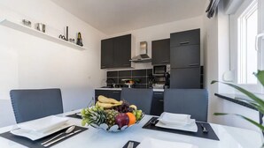 Een moderne keuken met donkere kastjes, een magnetron en een fruitschaal op de eettafel.