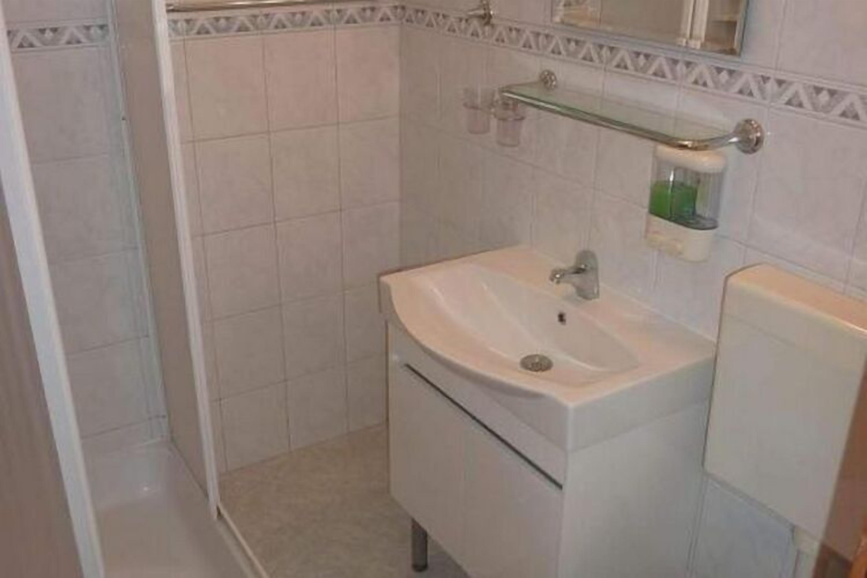 A bathroom with a white sink, mirror, and a glass shelf with toiletries.