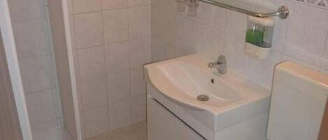 A bathroom with a white sink, mirror, and a glass shelf with toiletries.