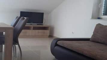 A modern living room with a dark sofa, a wooden TV stand, and a dining area with chairs.