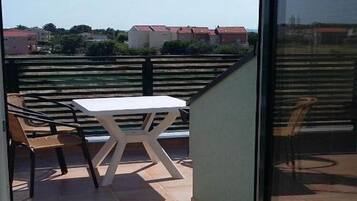 A balcony with a white table and chairs, overlooking a residential area.