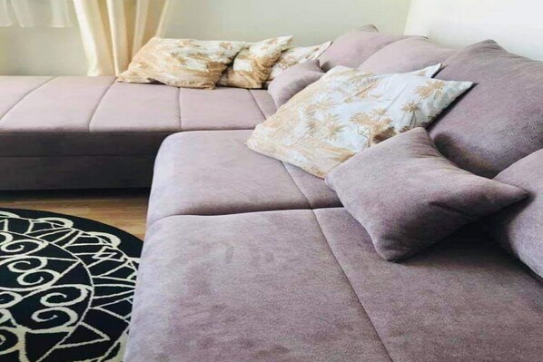 Una sala moderna con un amplio sofá en forma de L, varios cojines y un tapete estampado.