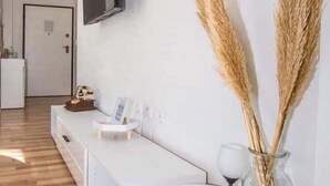 A modern living room with a white sofa, a glass vase with dried plants, and a small table with a picture frame and a candle.