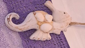 Un objeto decorativo que se asemeja a una criatura marina con conchas, sobre una superficie morada con textura.