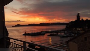 En kustutsikt med en solnedgång, en småbåtshamn och byggnader.