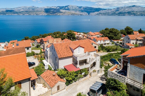 Un villaggio costiero con edifici a tetti in terracotta, vista limpida sul mare e montagne sullo sfondo.
