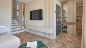 A modern hotel room with a flat-screen TV mounted on the wall, a built-in bench, a staircase, and a small kitchen area. - Apartment Blù-Two Bedroom Apartment with Terrace and Sea View (Dubrovnik)