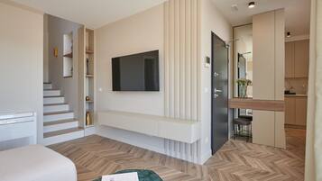 Une chambre d’hôtel moderne dotée d’un téléviseur à écran plat fixé au mur, d’une banquette intégrée, d’un escalier et d’un petit coin cuisine.