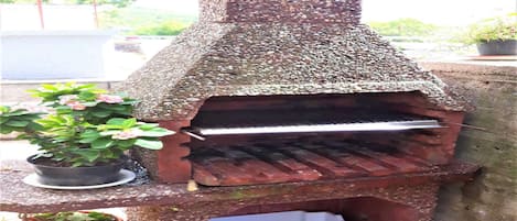 A stone-built outdoor oven with a metal shelf, surrounded by potted plants.