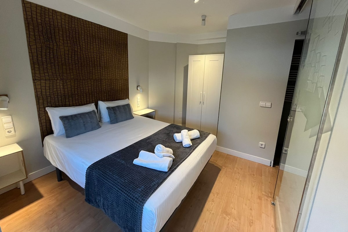 Una habitación de hotel moderna con una cama grande, un armario y cabina de ducha de vidrio.