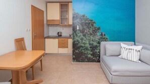 Um espaço de estar compacto com cozinha compacta, mesa de jantar, sofá e um grande mural na parede retratando uma floresta e céu azul.