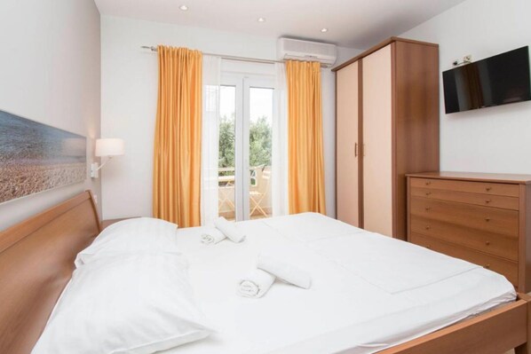A hotel room with a bed, a wooden wardrobe, a television, and a balcony with yellow curtains. - Apartments Antonio - Studio with Balcony (2+1) - 5 (Tucepi)