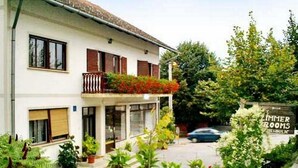 Un immeuble de deux étages doté d’un balcon, de plantes en pot et d’une enseigne indiquant « Zimmer Rooms ».
