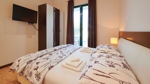 Une chambre d’hôtel avec deux lits, un téléviseur à écran plat fixé au mur, une fenêtre avec des rideaux et une lampe de chevet.