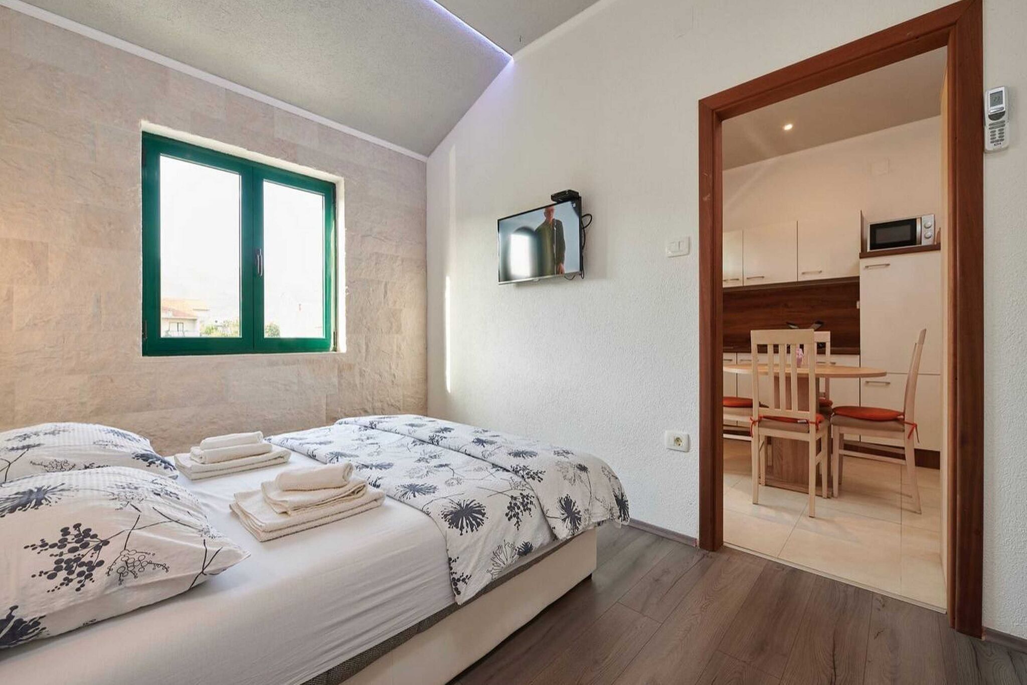 Une chambre à coucher comprenant un lit, un téléviseur fixé au mur, une fenêtre et une vue sur un coin repas.
