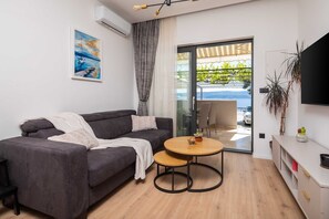 A modern living room with a grey sofa, a round wooden table, and a large TV.