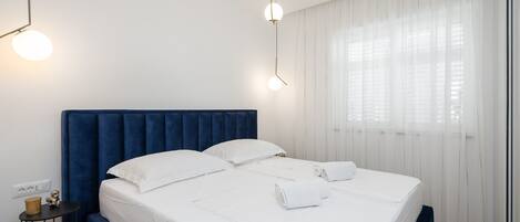 A neatly made bed with white linens and two pillows, a blue headboard, and a bedside table with a lamp.