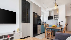 Une cuisine moderne avec un réfrigérateur noir, un coin repas avec une table et des chaises en bois, et un téléviseur à écran plat fixé au mur.