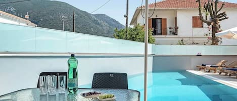 A poolside area with a glass table, chairs, and a bottle of water.
