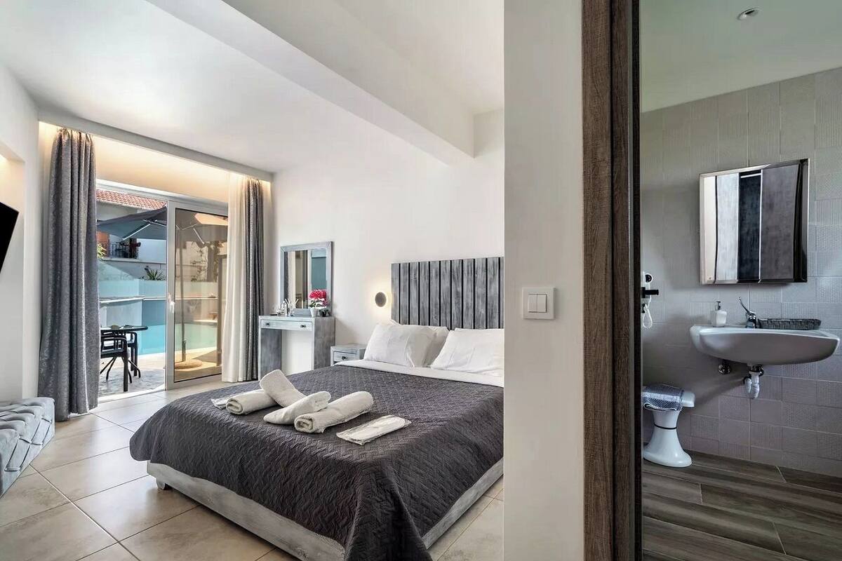 A modern hotel room with a large bed, a bedside table, a mirror, and a bathroom with a sink and toilet.