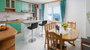 Une cuisine moderne avec des meubles de couleur verte, un îlot central doté de tabourets de bar et un coin repas avec une table dressée pour deux personnes.