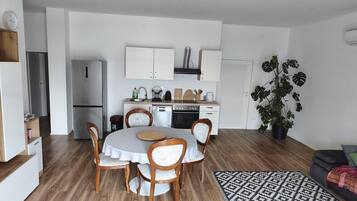 A modern kitchen with white cabinets, a dining table with chairs, and a large plant.
