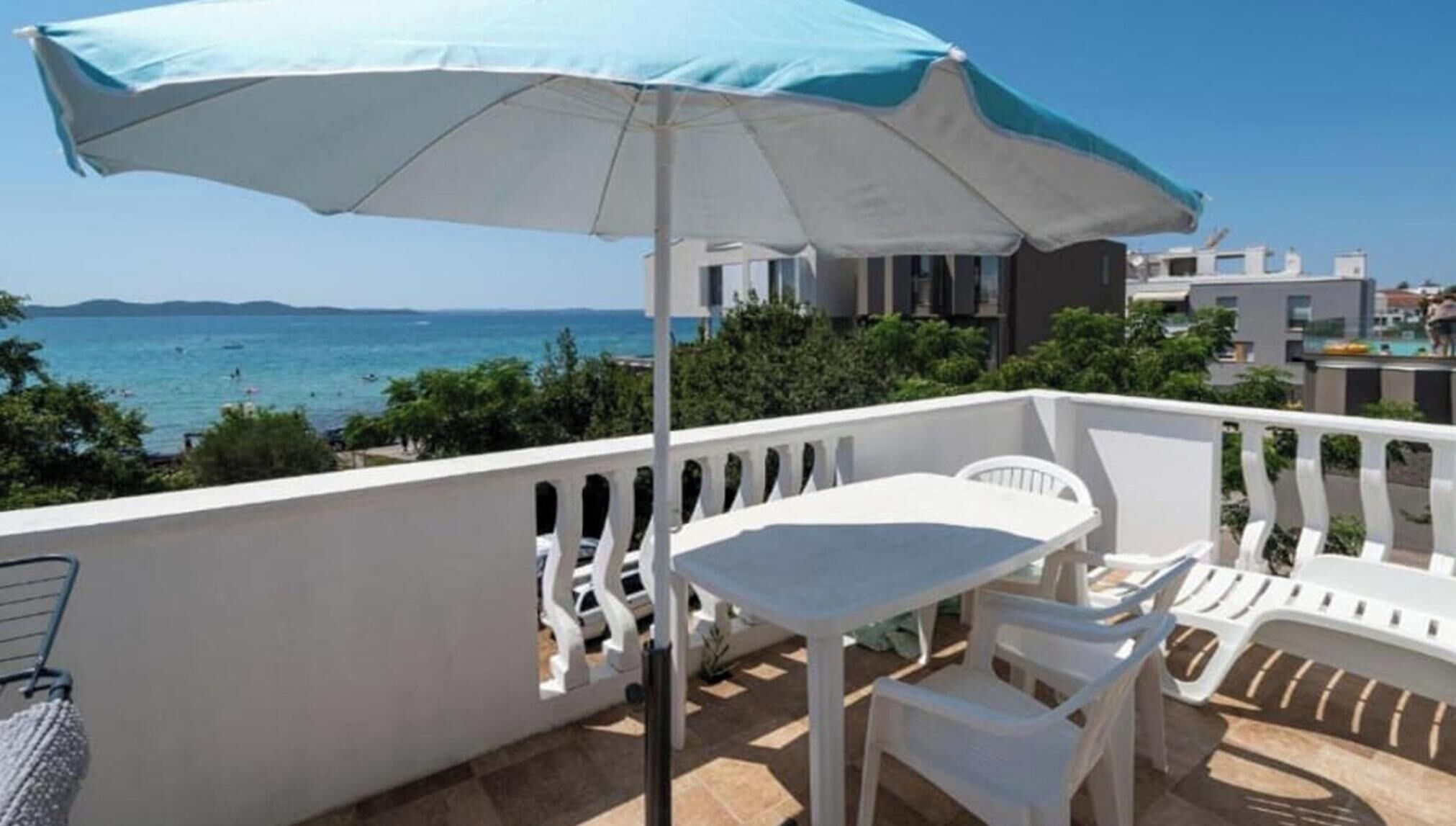 A balcony with a table and chairs, a white umbrella, and a view of the sea.
