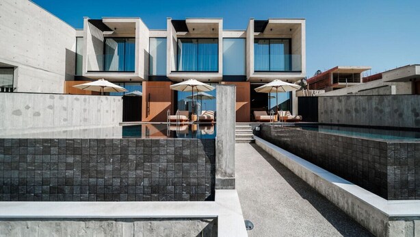 A modern building with a pool area, featuring multiple lounge chairs and umbrellas. - Stylish Townhouse with stunning sea view and pool (Chlorakas)