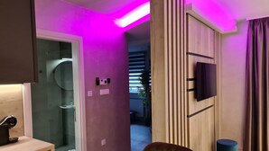 Une salle de bain moderne avec une douche à parois de verre, un meuble-lavabo avec un miroir et un mur éclairé en rose.