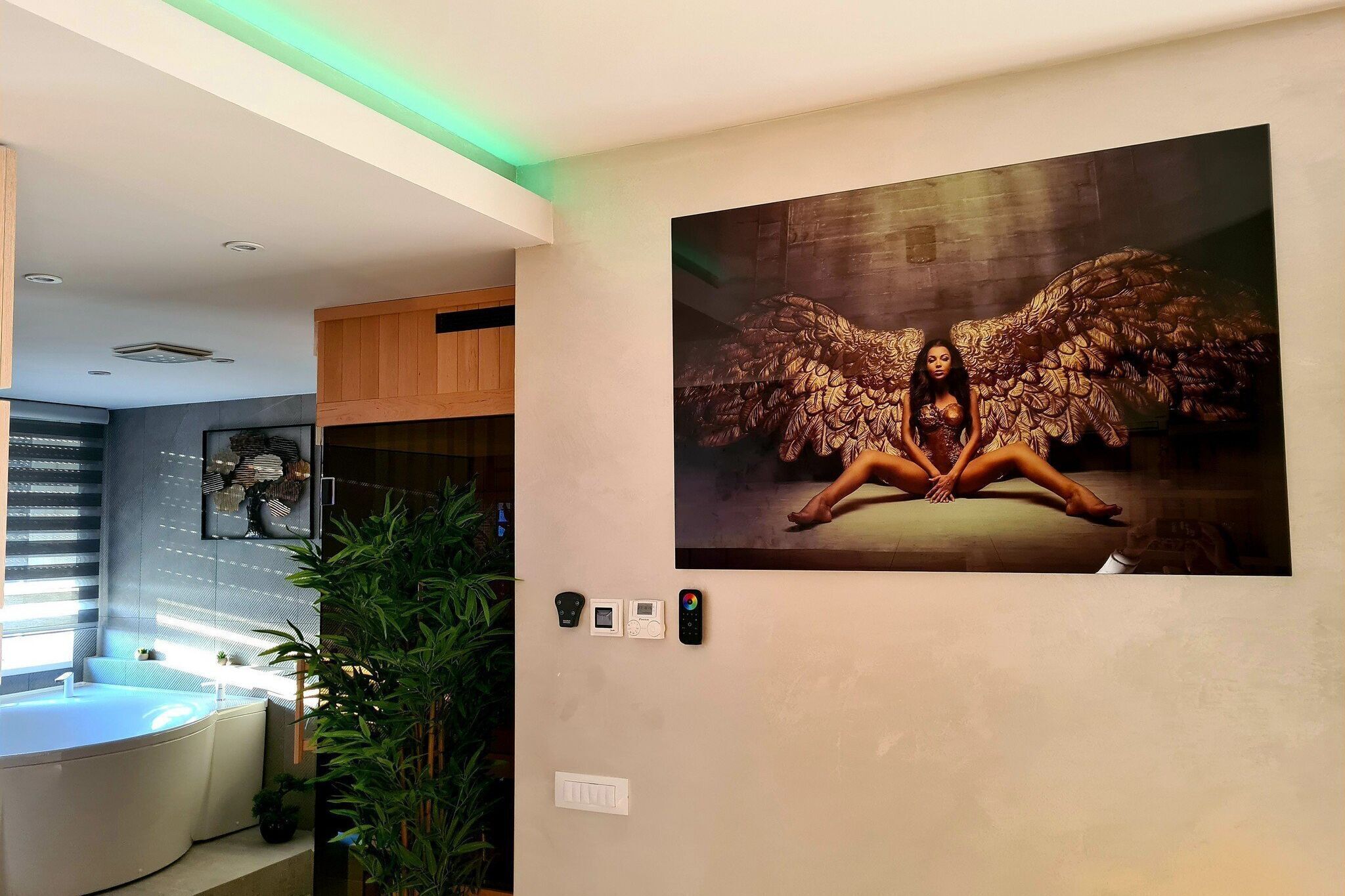 A modern bathroom with a large bathtub, a wall-mounted artwork of a woman with wings, and a green-lit ceiling.